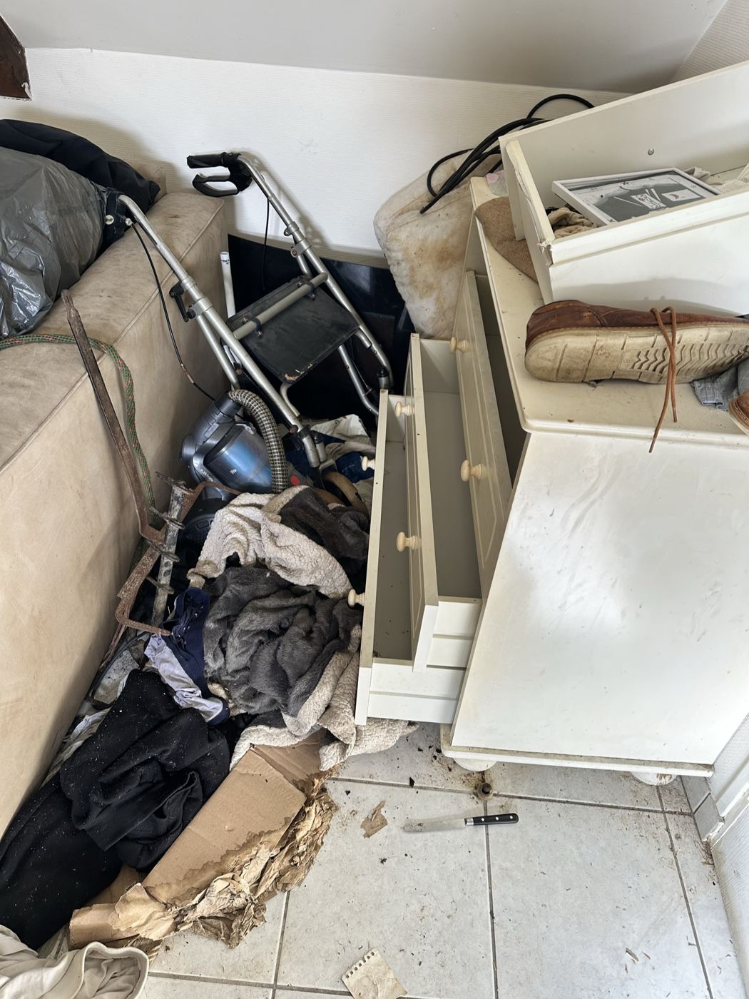 Commode et vêtements au sol dans un logement envahi, avant tri en cartons